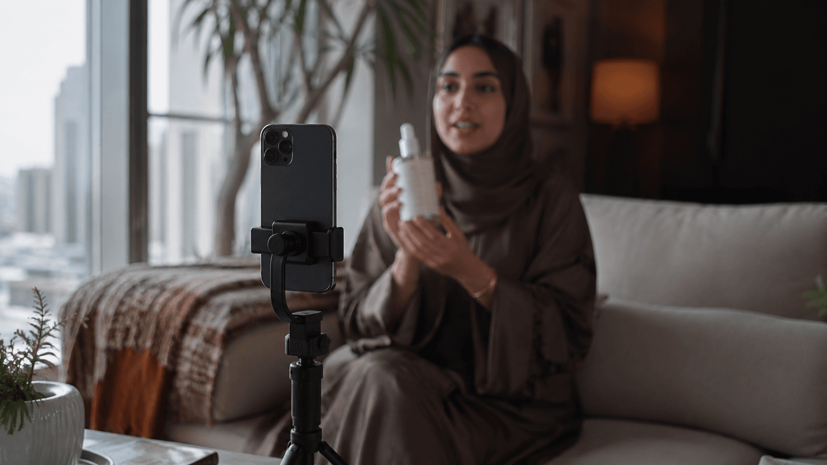 A creator filming a skincare product review on a phone mounted to a small tripod in a bright Riyadh living room